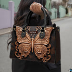 Gilded rose gold butterfly handbag standing upright on reflective marble flooring beside an ornate gift box.