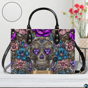 Jeweled skull handbag on white wooden table beside floral vase with texture swatch inset.