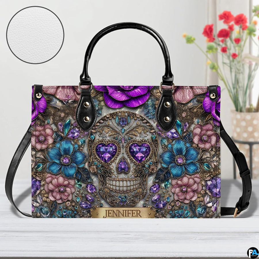 Jeweled skull handbag on white wooden table beside floral vase with texture swatch inset.