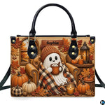 Front view of autumn satchel with embossed ghost in beanie sipping cocoa in armchair with pumpkins and candles.