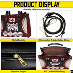 Side profile view of structured baseball handbag showing sleek silhouette and black carrying handles.