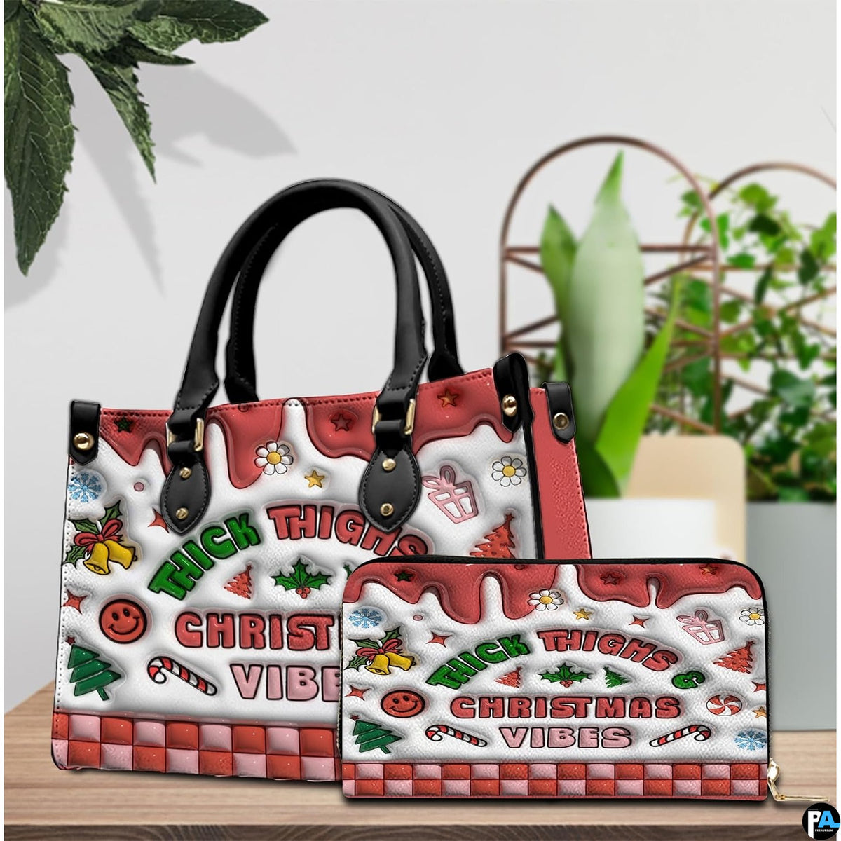 Handbag and matching zip wallet displayed on a wooden surface beside decorative potted greenery.