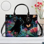 Front view of whimsical black cat art on white wooden surface beside red floral vase.