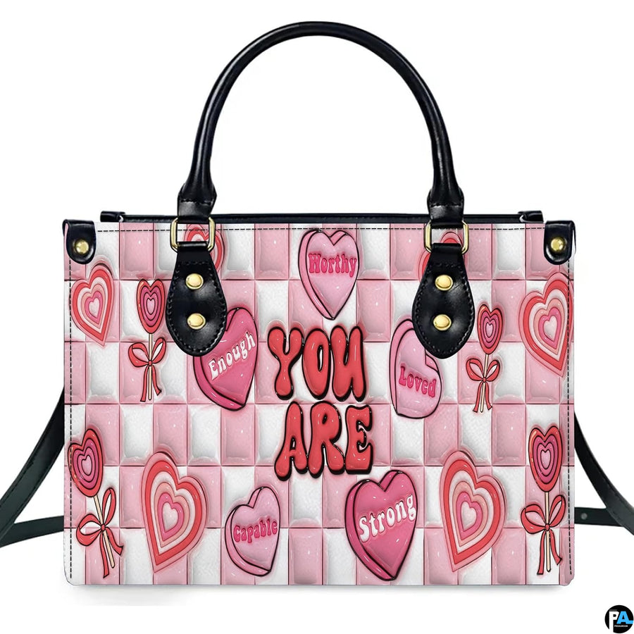 Front view of pink affirmation handbag showing conversation candy hearts on checkerboard ground.
