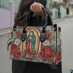 Model wearing Our Lady of Guadalupe handbag over shoulder with attached strap.