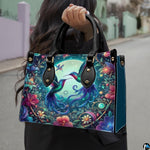 Model holding handbag outdoors showcasing twin hummingbirds and glowing moonlit botanical artwork.