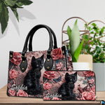 Sculpted black cat and floral artwork displayed on a wooden surface beside house plants.