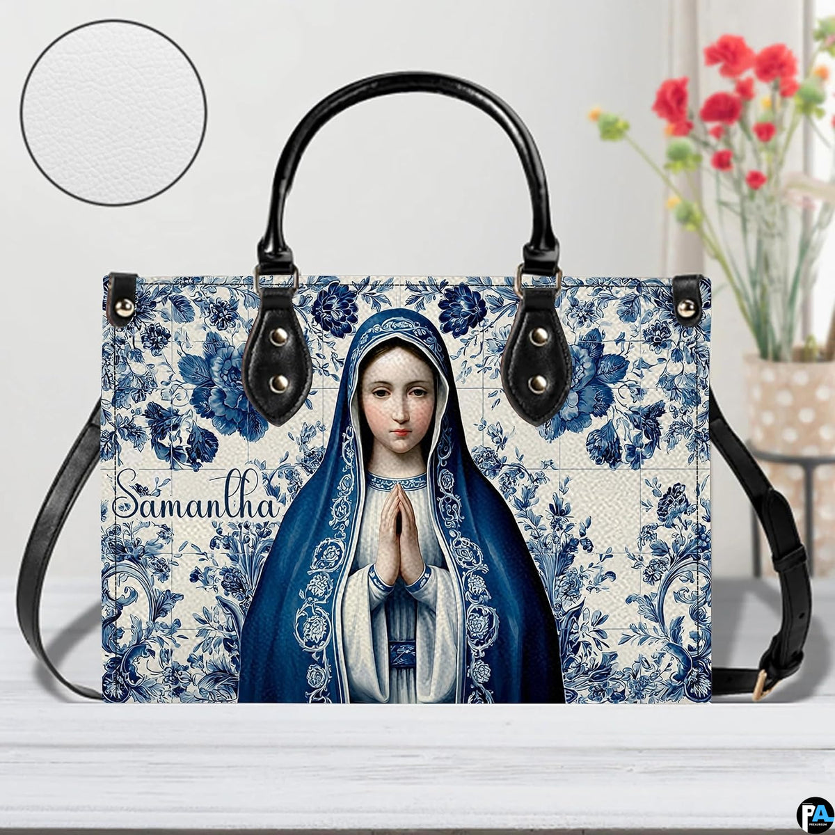 Praying Virgin Mary handbag beside floral vase with circular texture detail.