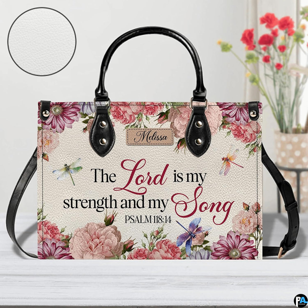 Scripture floral dragonfly handbag displayed on white table beside floral bouquet.