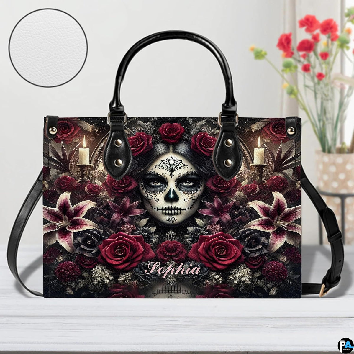 Sugar skull handbag displayed on white table beside floral bouquet.