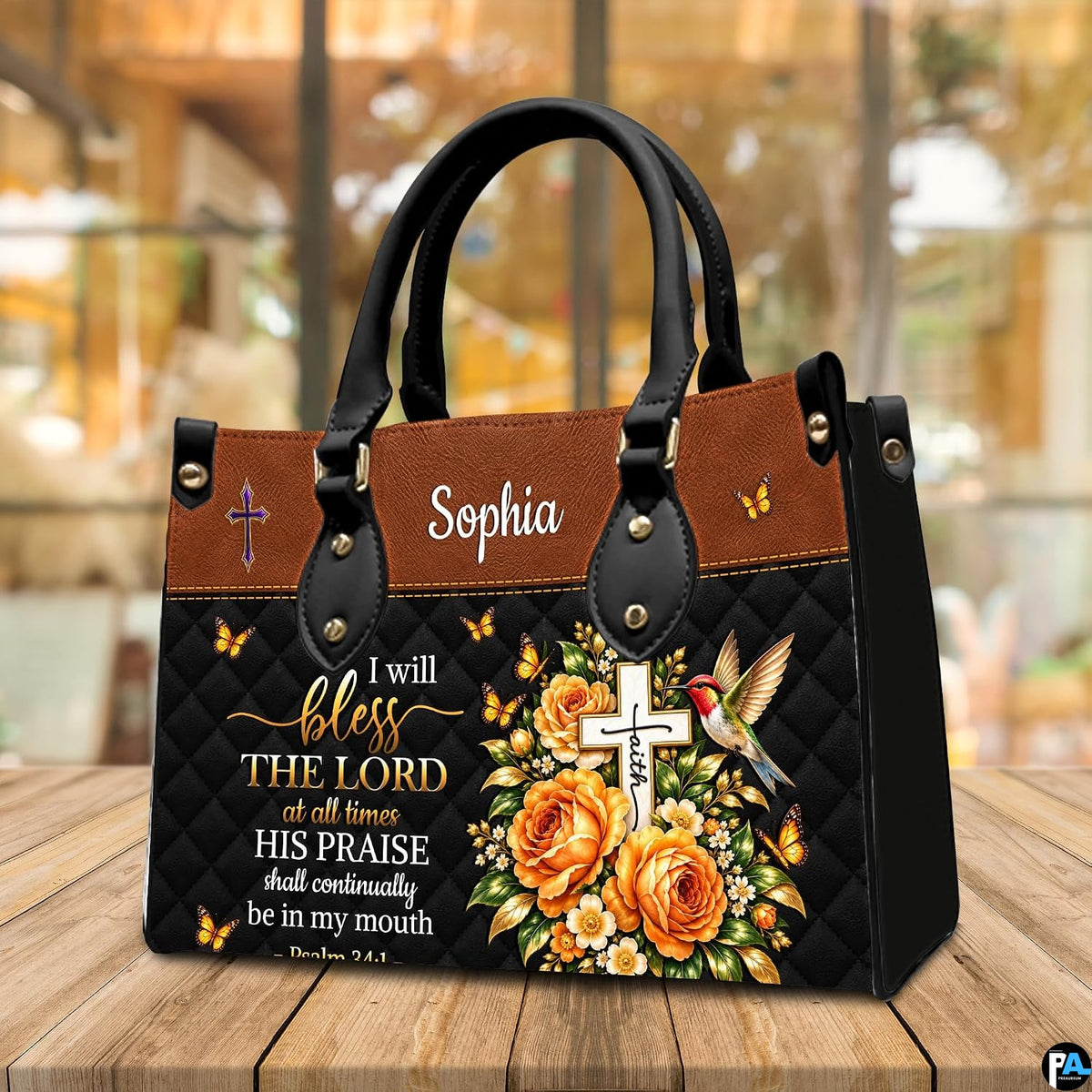 Hummingbird cross handbag displayed on wooden tabletop in front of sunlit cafe window.