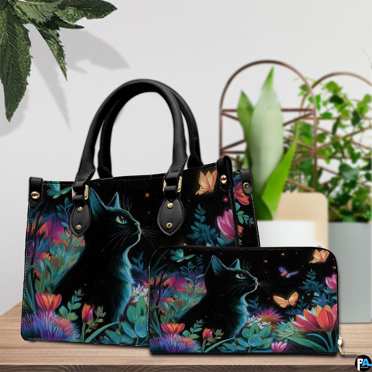 Tabletop presentation showing black cat flowers art on wood beside green houseplants.