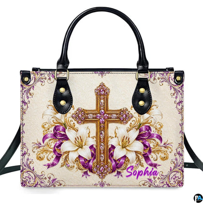 Devotional handbag displaying a jeweled golden cross with purple crystals, white lilies, and purple ribbons.