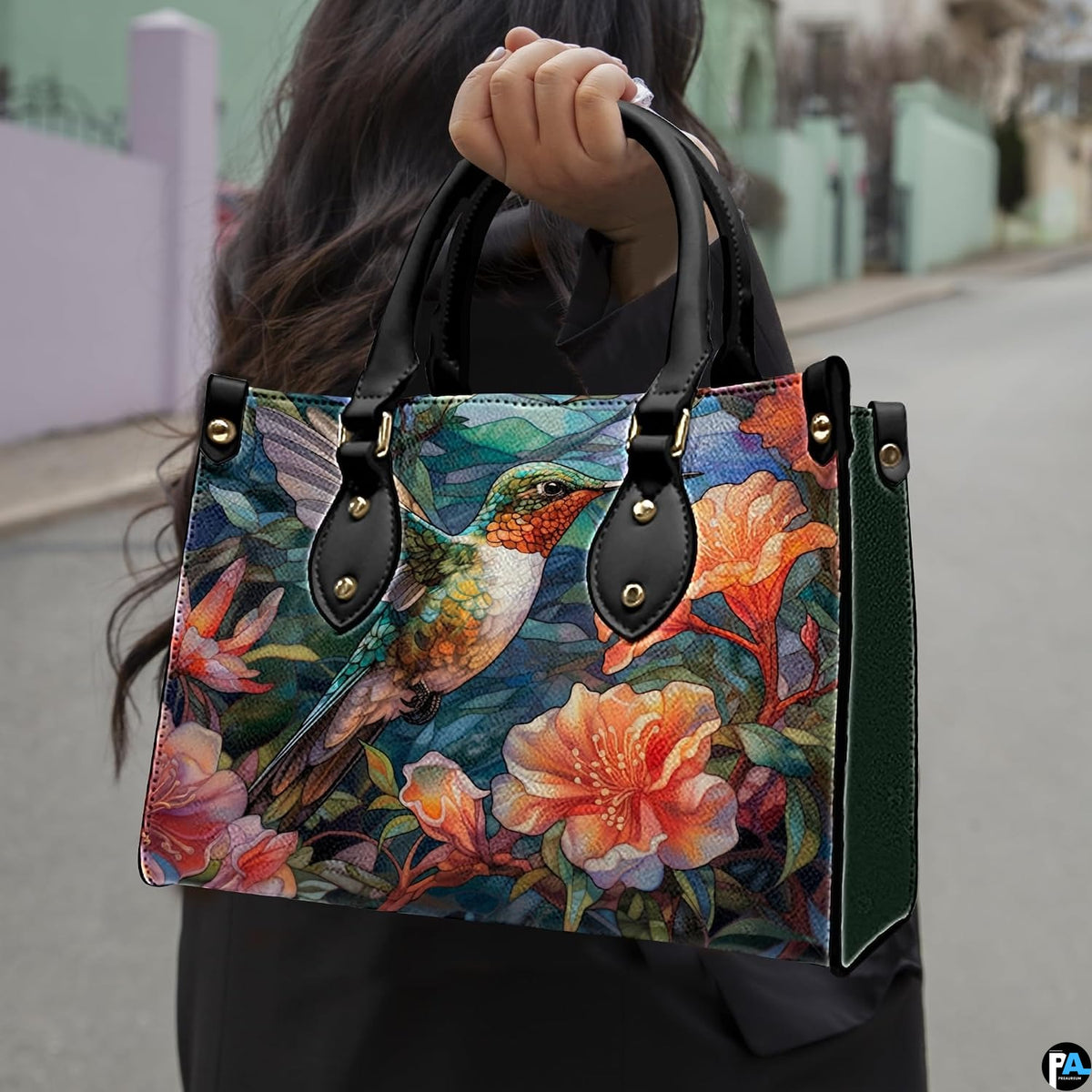 Model holding mosaic hummingbird handbag outdoors showcasing vibrant avian and botanical floral artwork.