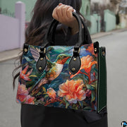 Model holding mosaic hummingbird handbag outdoors showcasing vibrant avian and botanical floral artwork.