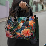 Model holding mosaic hummingbird handbag outdoors showcasing vibrant avian and botanical floral artwork.