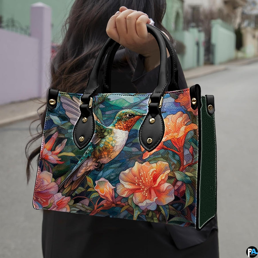 Model holding mosaic hummingbird handbag outdoors showcasing vibrant avian and botanical floral artwork.