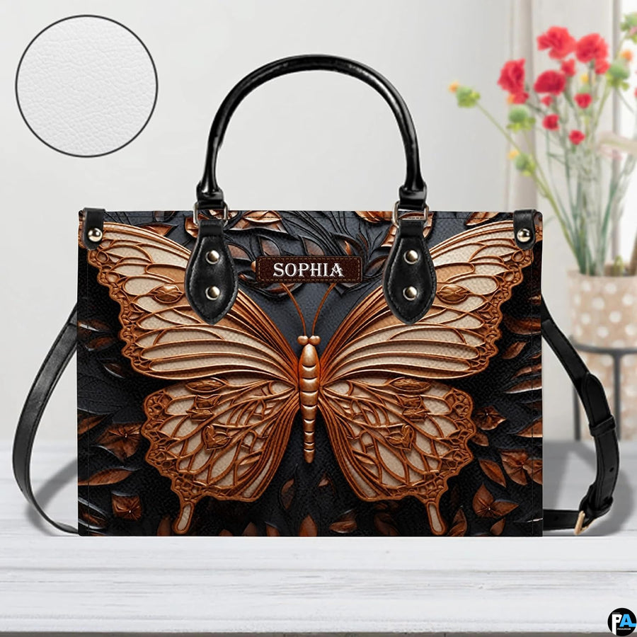 Sculpted bronze butterfly handbag shown on a white tabletop with floral decor.