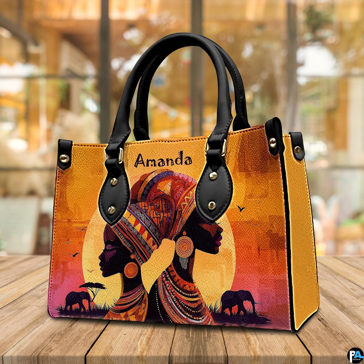 African sunset artwork presented resting on a wooden cafe tabletop against a blurred indoor setting.