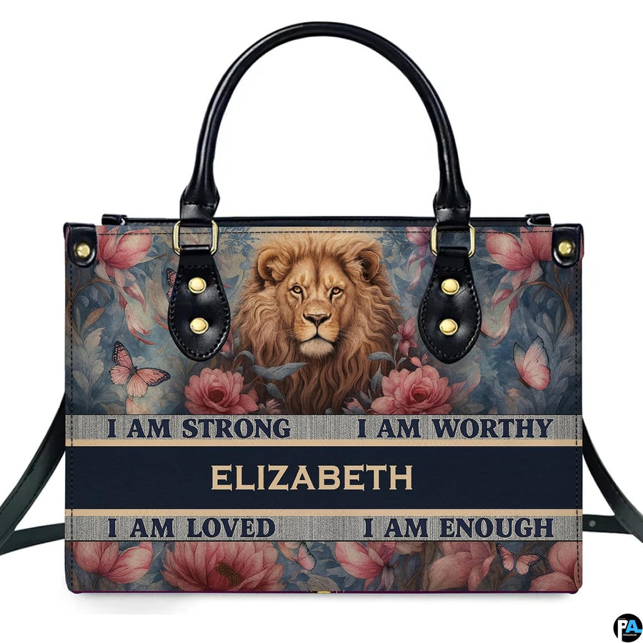 Frontal view of handbag featuring a painted lion portrait amidst vintage pink roses, butterflies, and affirmation banners.
