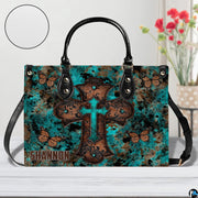 Front view of turquoise cross butterfly handbag showing central cross and monarch butterflies.