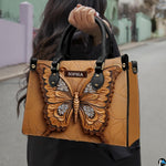 Outdoor street view of a model carrying the sculpted tan butterfly handbag by its top handles.