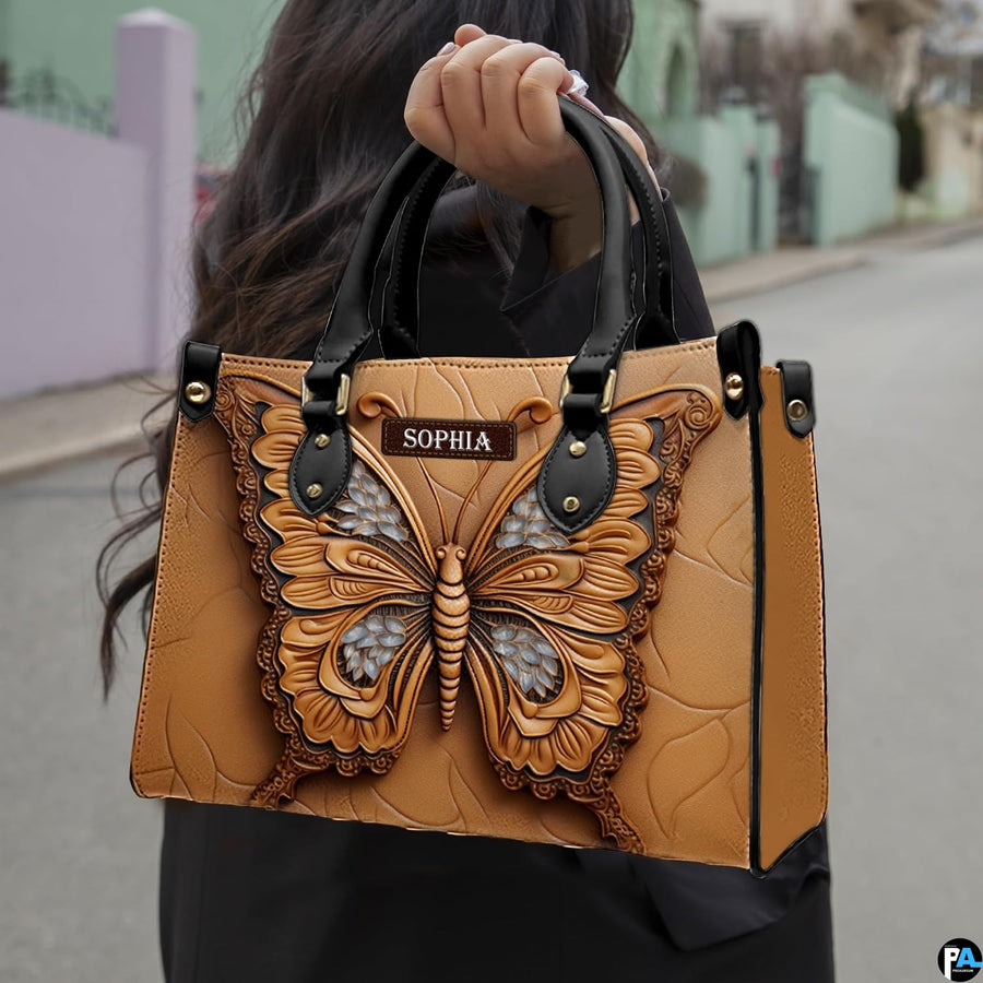 Outdoor street view of a model carrying the sculpted tan butterfly handbag by its top handles.