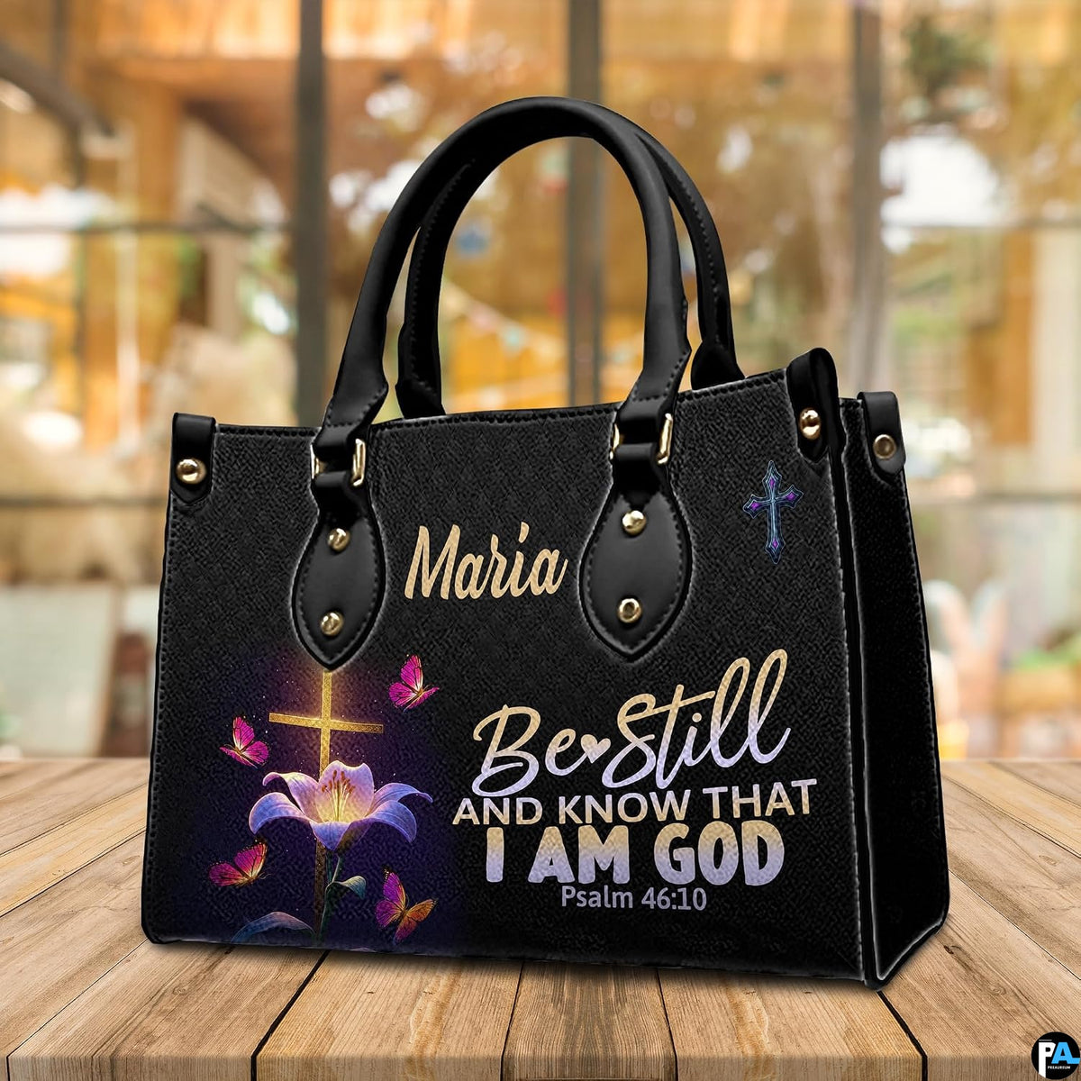 Illuminated cross and lily handbag resting on a wooden tabletop in a bright indoor room.