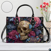 Filigree skull handbag on white wooden table beside floral vase with texture swatch inset.