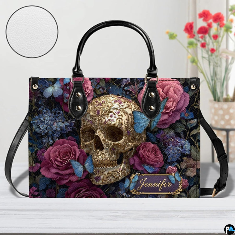 Filigree skull handbag on white wooden table beside floral vase with texture swatch inset.