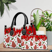 Tabletop staging of festive handbag and coordinating wallet displaying gingerbread tree and red drip artwork.