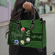 Front view of green handbag featuring contoured heart outline, watercolor garden blossoms, and pulse line.