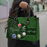 Front view of green handbag featuring contoured heart outline, watercolor garden blossoms, and pulse line.