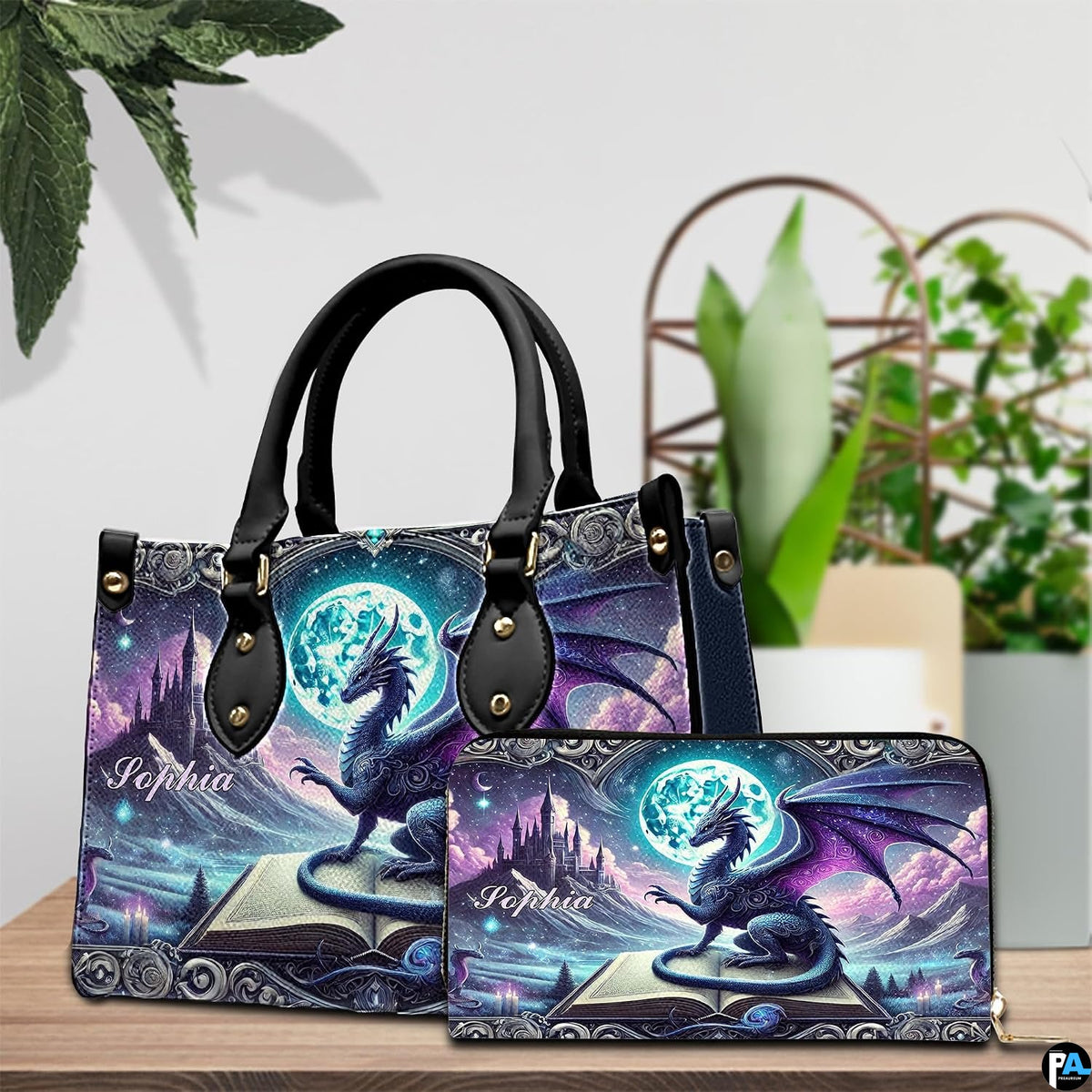 Matching dragon fantasy handbag and zip wallet on table beside indoor houseplant.