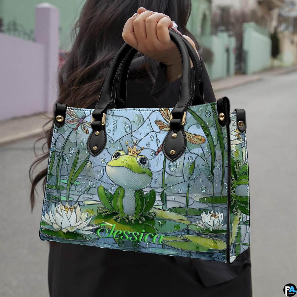 Front view of frog prince handbag showing crowned frog, white water lilies, and dragonflies.