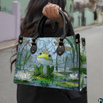 Front view of frog prince handbag showing crowned frog, white water lilies, and dragonflies.