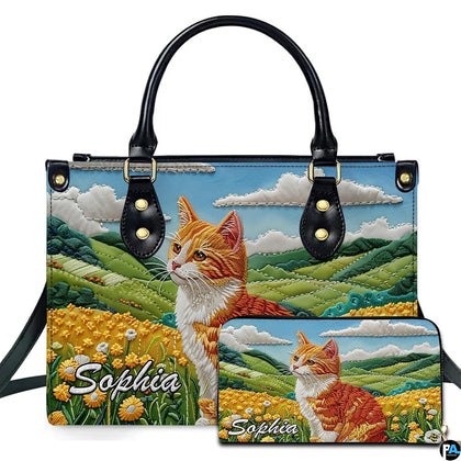 Embroidered ginger tabby cat seated in a yellow buttercup meadow beside rolling green hills.