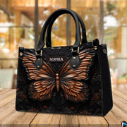 Copper butterfly handbag displayed on a wooden outdoor deck in front of sunlit cafe windows.