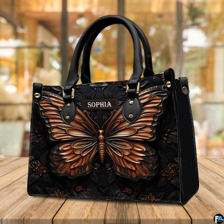 Copper butterfly handbag displayed on a wooden outdoor deck in front of sunlit cafe windows.