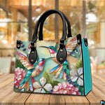 Back view of mosaic hummingbird handbag showing continuous colorful print on white background.