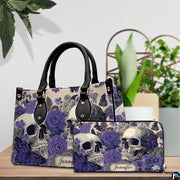 Violet skull handbag and matching wallet displayed on wooden table beside potted plant.