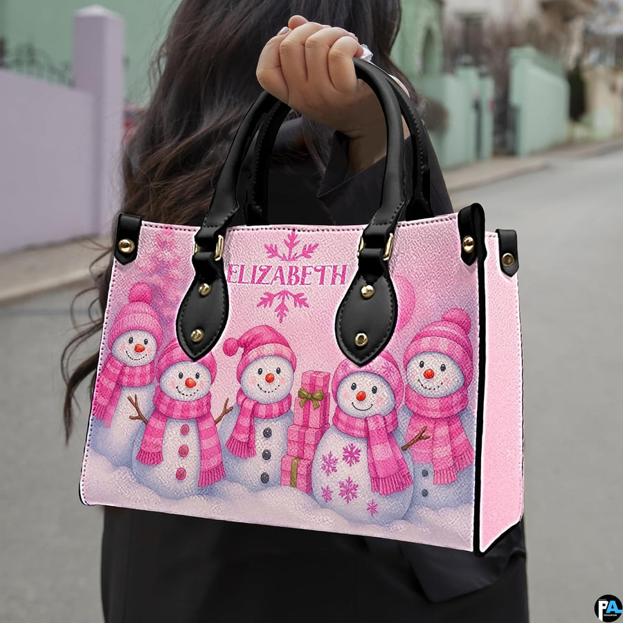 Model holding the pink snowman handbag by dual top handles outdoors, displaying size and carrying style.