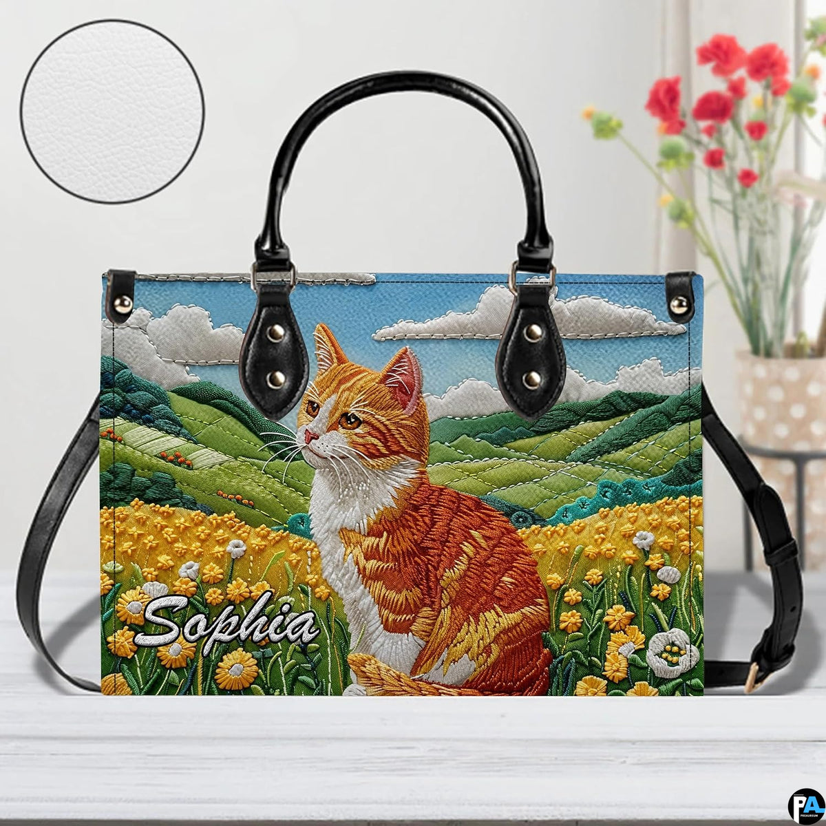 Studio display of embroidered orange tabby cat and rolling meadow hills artwork.