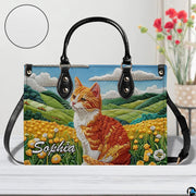 Studio display of embroidered orange tabby cat and rolling meadow hills artwork.