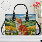 Studio display of embroidered orange tabby cat and rolling meadow hills artwork.