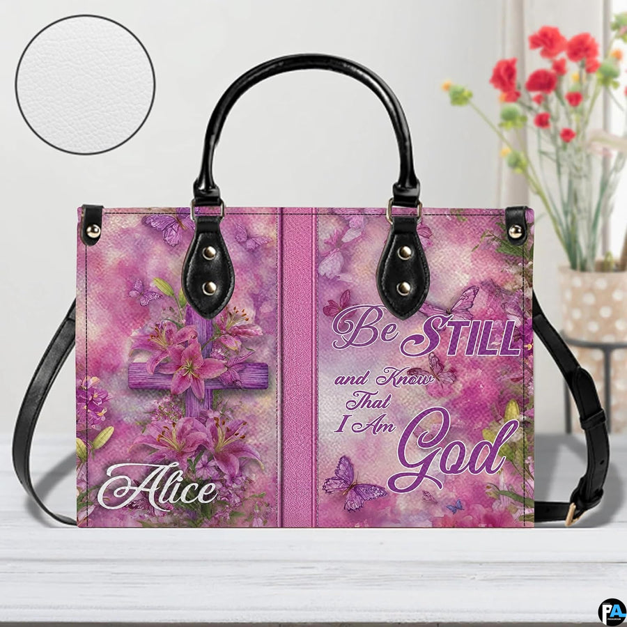 Front view of pink handbag featuring wooden cross draped with blooming lilies and flying butterflies.