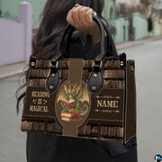 Model carrying spectacled dragon handbag by top handles while walking along an outdoor street