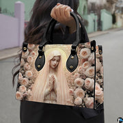 Model wearing dark coat carrying the blush rose Virgin Mary handbag over her shoulder outdoors.