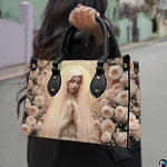 Model wearing dark coat carrying the blush rose Virgin Mary handbag over her shoulder outdoors.