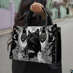 Gothic black cat handbag held by top handle while walking outdoors along a residential street.